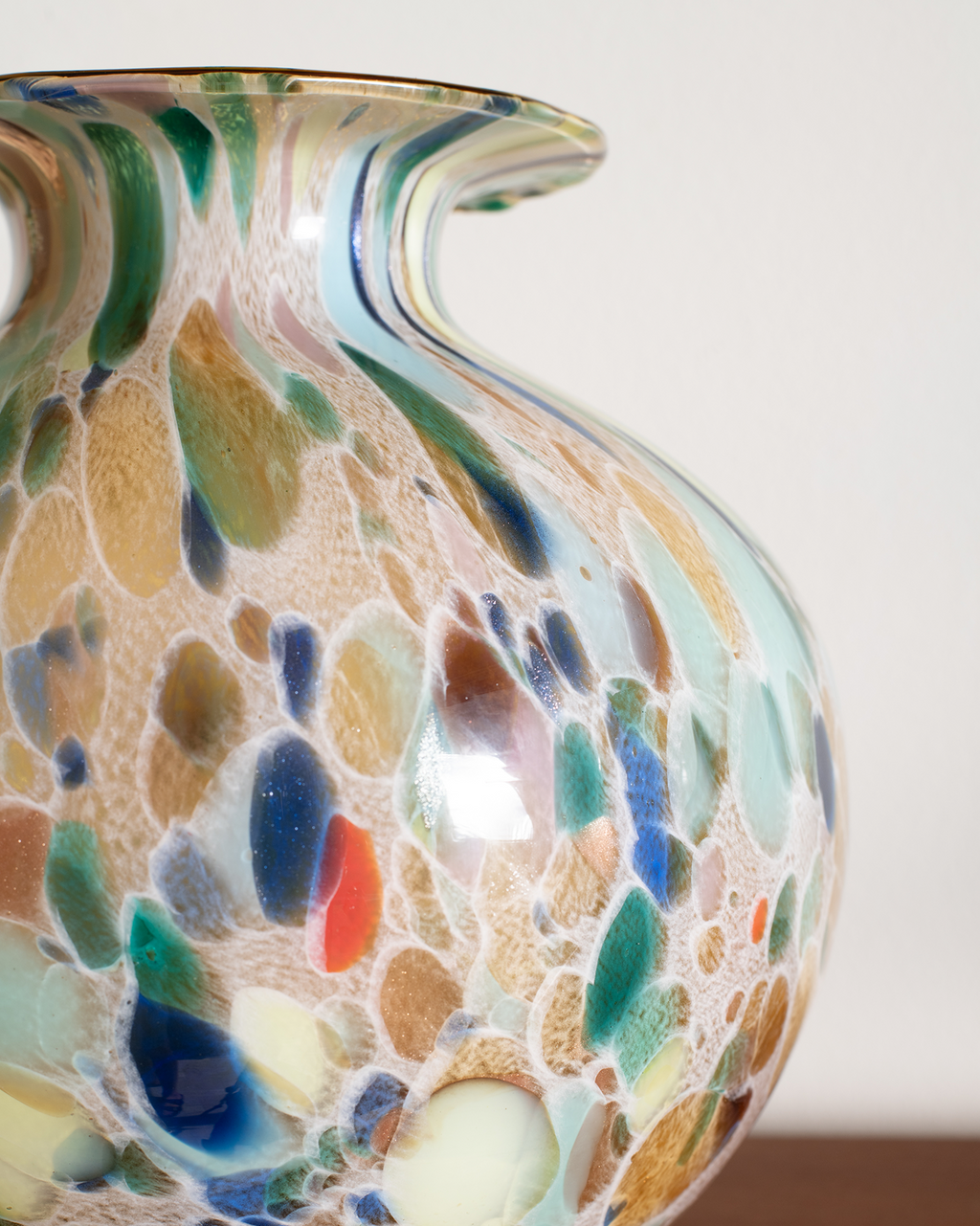 Close-up of a decorative glass vase with a multicolor spotted pattern in blue, green, gold, and red on a white background.