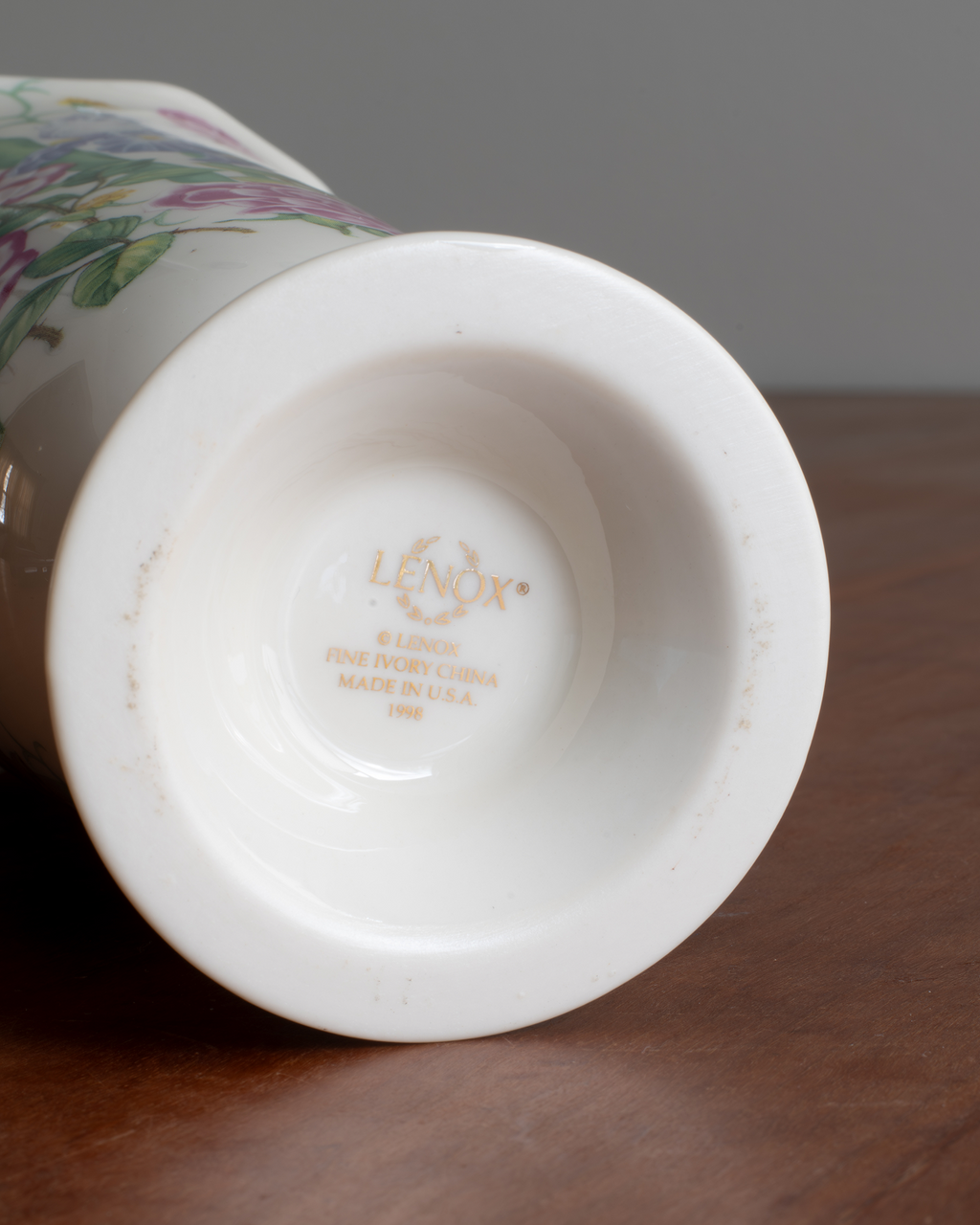 Close-up of the bottom interior of a white porcelain vase, showing the brand name 'LENOX' printed in gold, resting on a dark brown wooden surface.