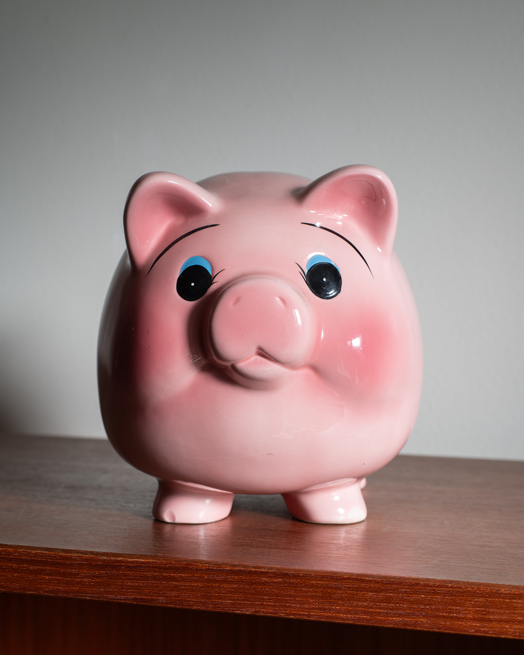 A glossy pink piggy bank shaped like a pig, standing on a wooden surface against a plain light gray background.