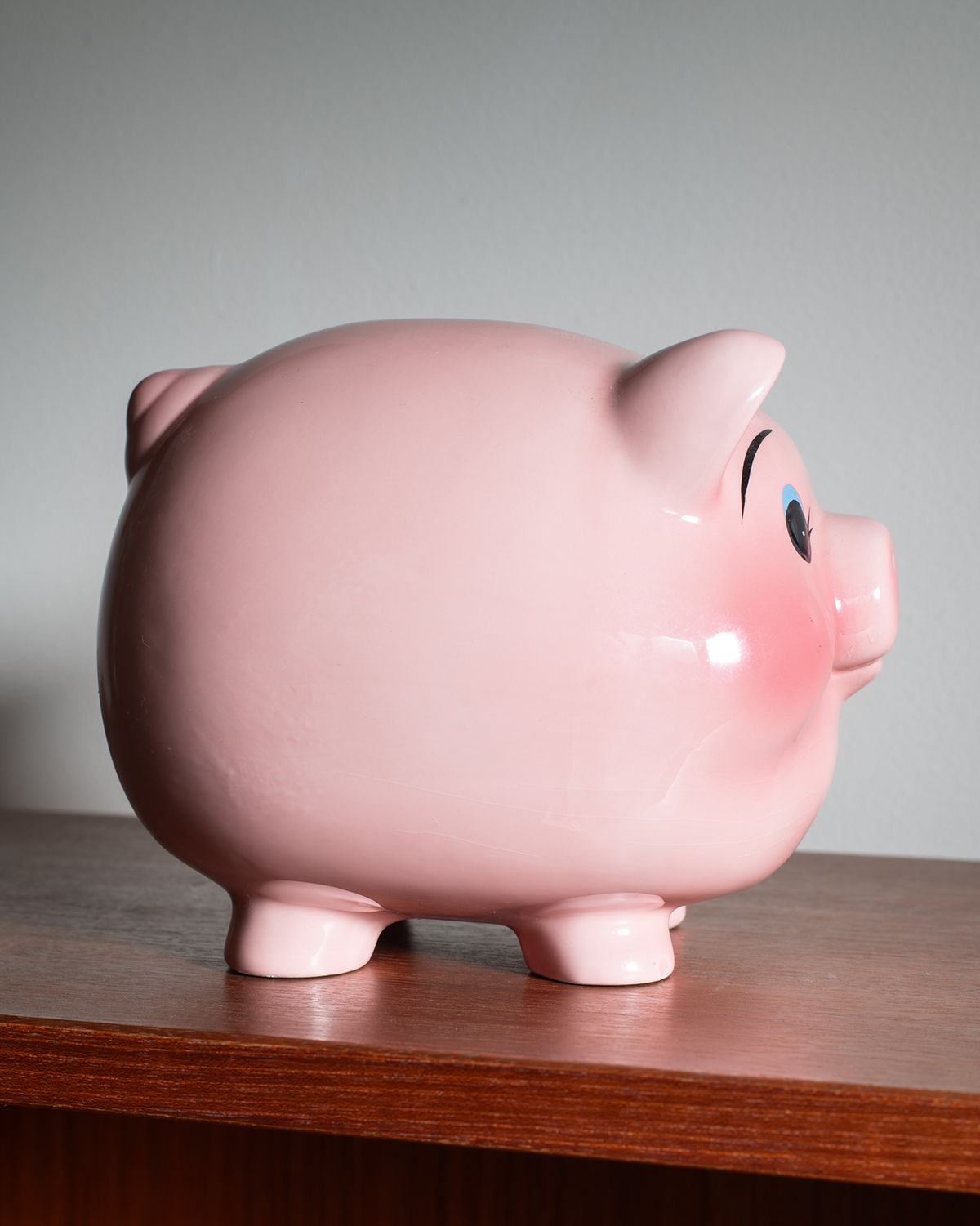 A glossy pink piggy bank shaped like a pig, standing on a wooden surface against a plain light gray background.