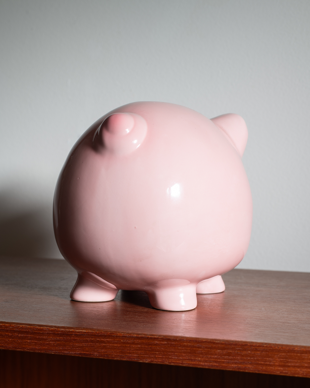 A glossy pink piggy bank shaped like a pig, standing on a wooden surface against a plain light gray background.