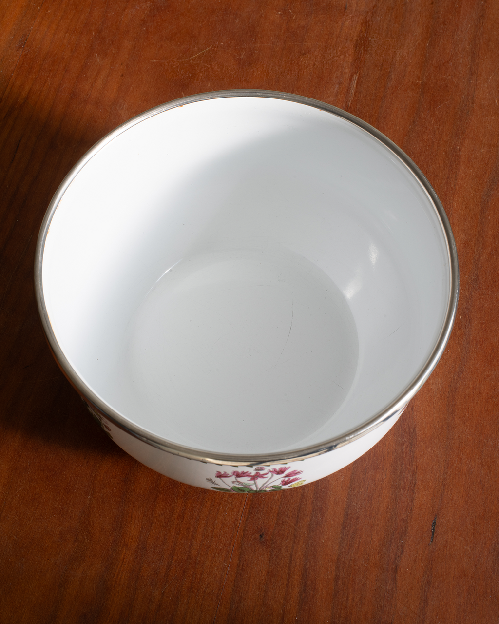 A white ceramic bowl with a silver rim and a small floral pattern near the base, shown on a wooden table.