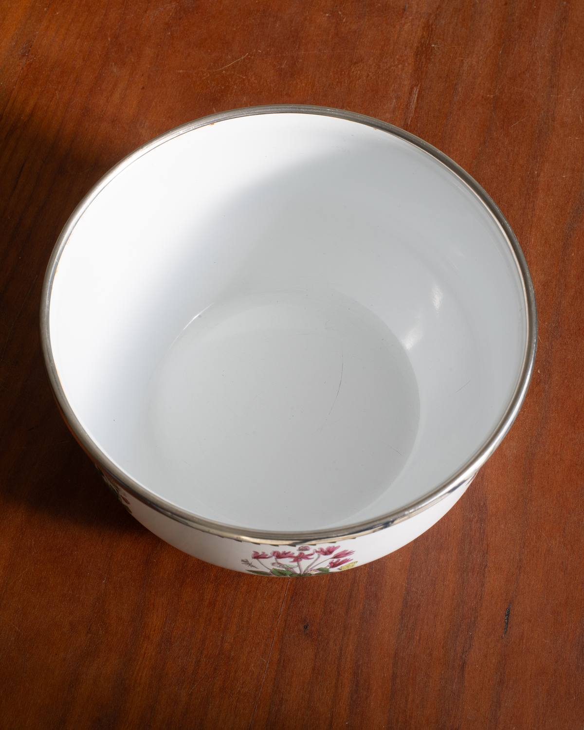 A white ceramic bowl with a silver rim and a small floral pattern near the base, shown on a wooden table.