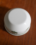 A white ceramic bowl with a green floral pattern around the rim, photographed upside down on a brown wooden surface.