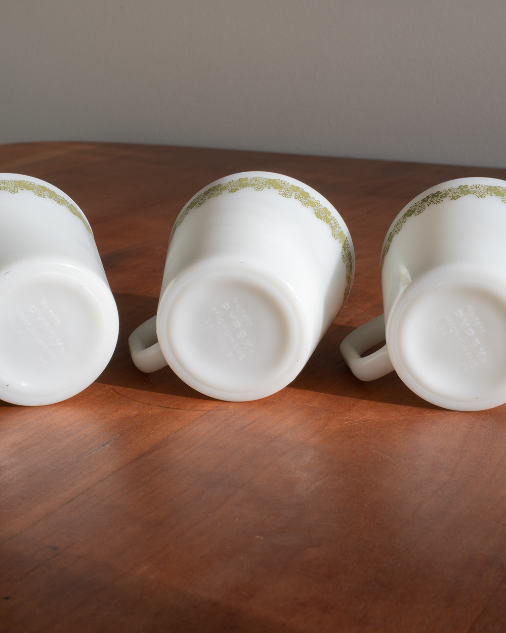 Three white mugs with a delicate gold patterned band near the rim, shown upside down on a wooden tabletop.