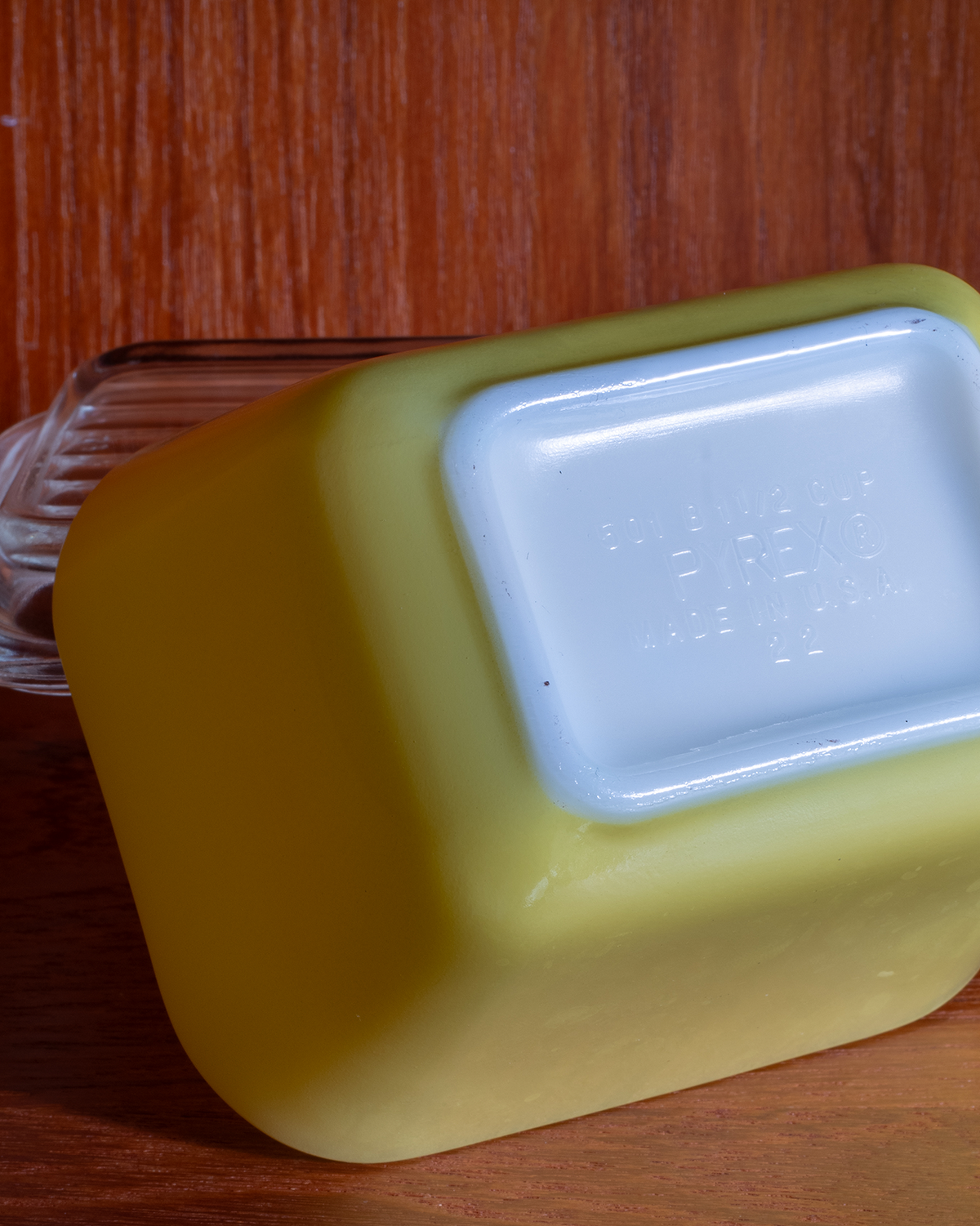 A yellow plastic container with a white square label on its side, photographed on a wooden surface.