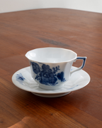 A white porcelain teacup and saucer set decorated with a blue floral pattern, placed on a wooden table.