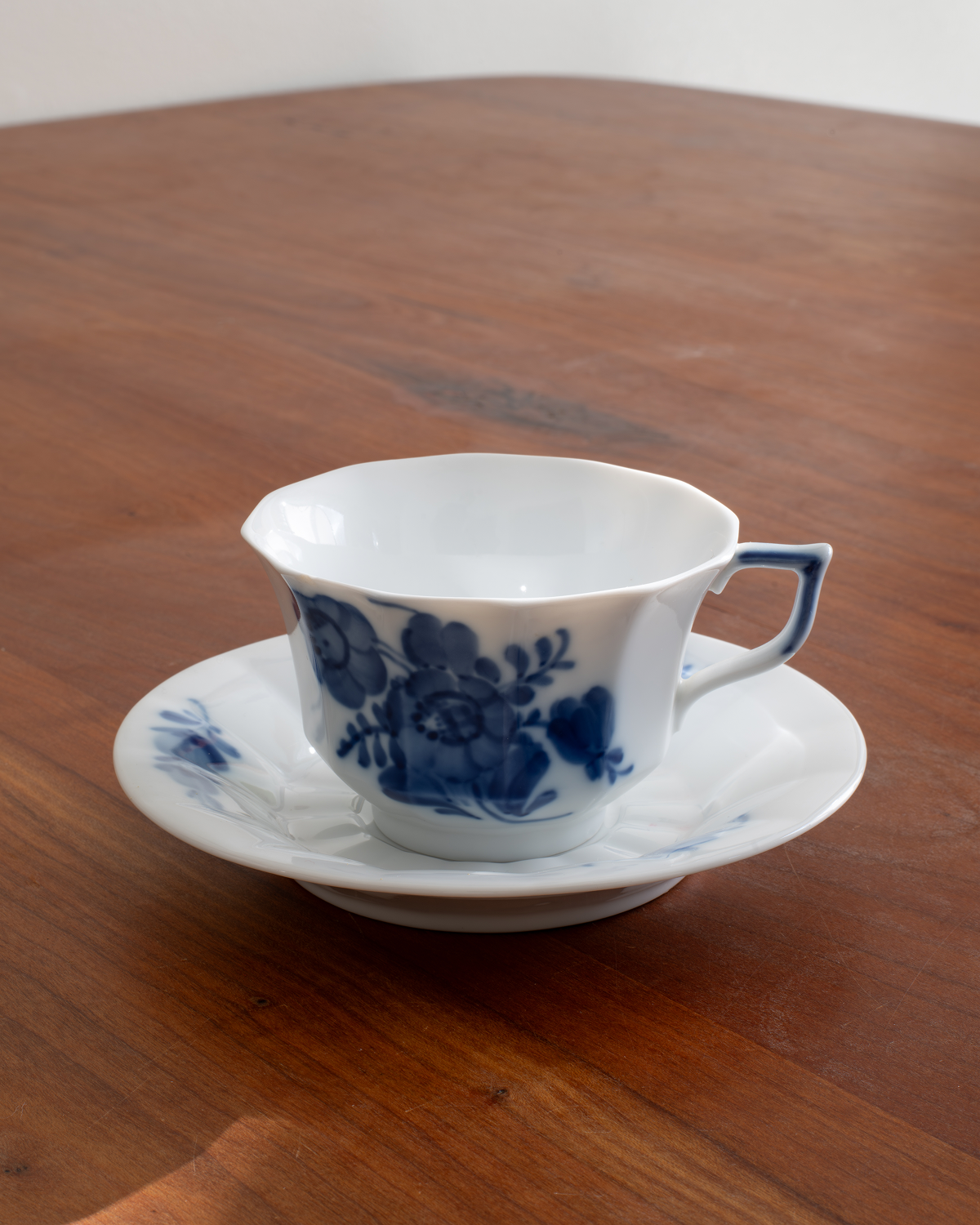 A white porcelain teacup and saucer set decorated with a blue floral pattern, placed on a wooden table.